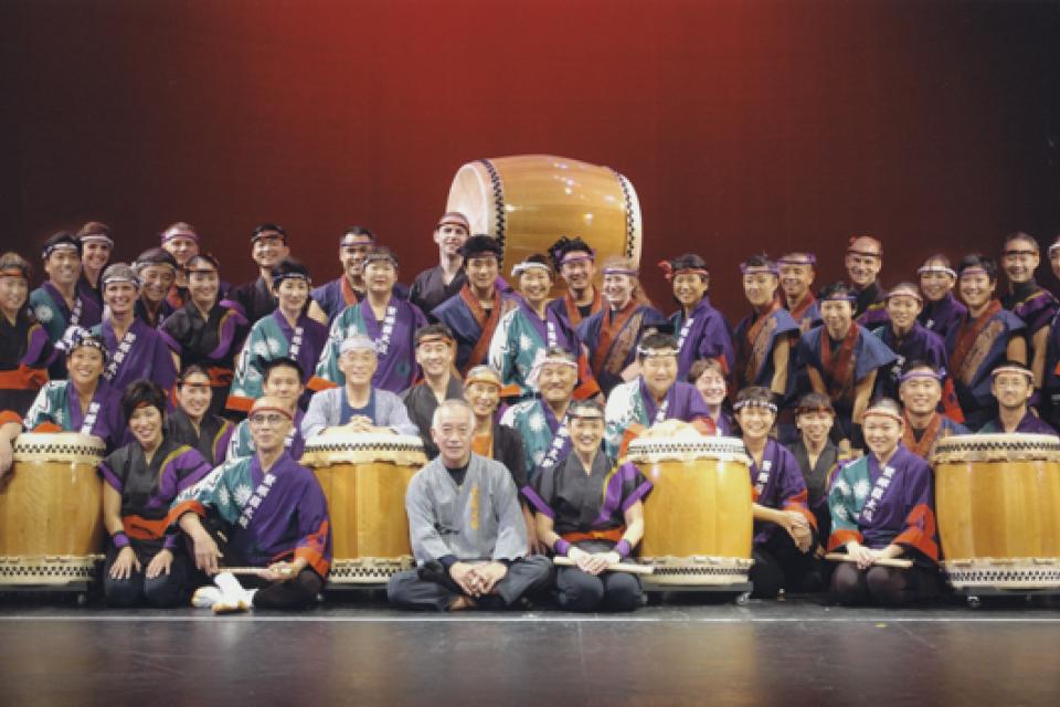 Multiple taiko groups gather for a photo onstage with drums